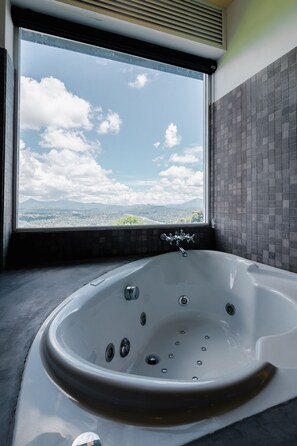 A modern bathroom with a large bathtub, a view of the sky and clouds, and a tiled wall.
