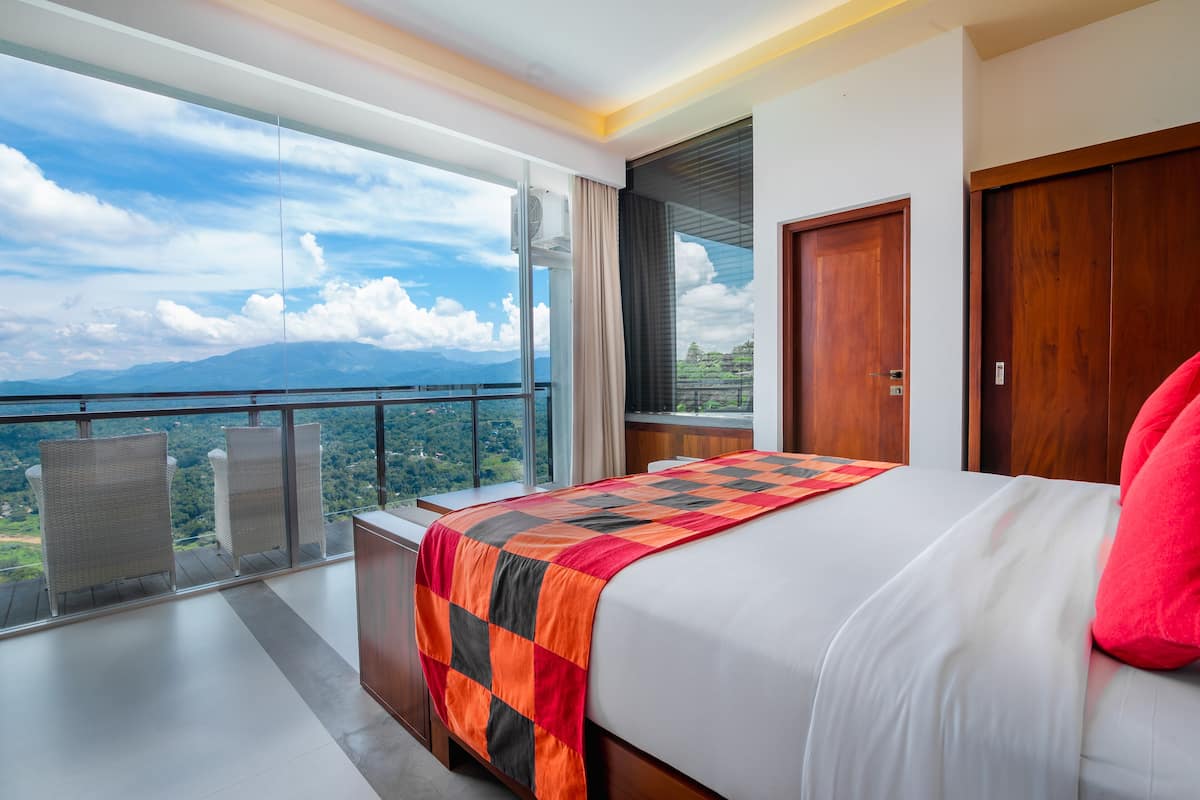 A bedroom with a large bed, a view of the mountains, and a balcony with wicker chairs.