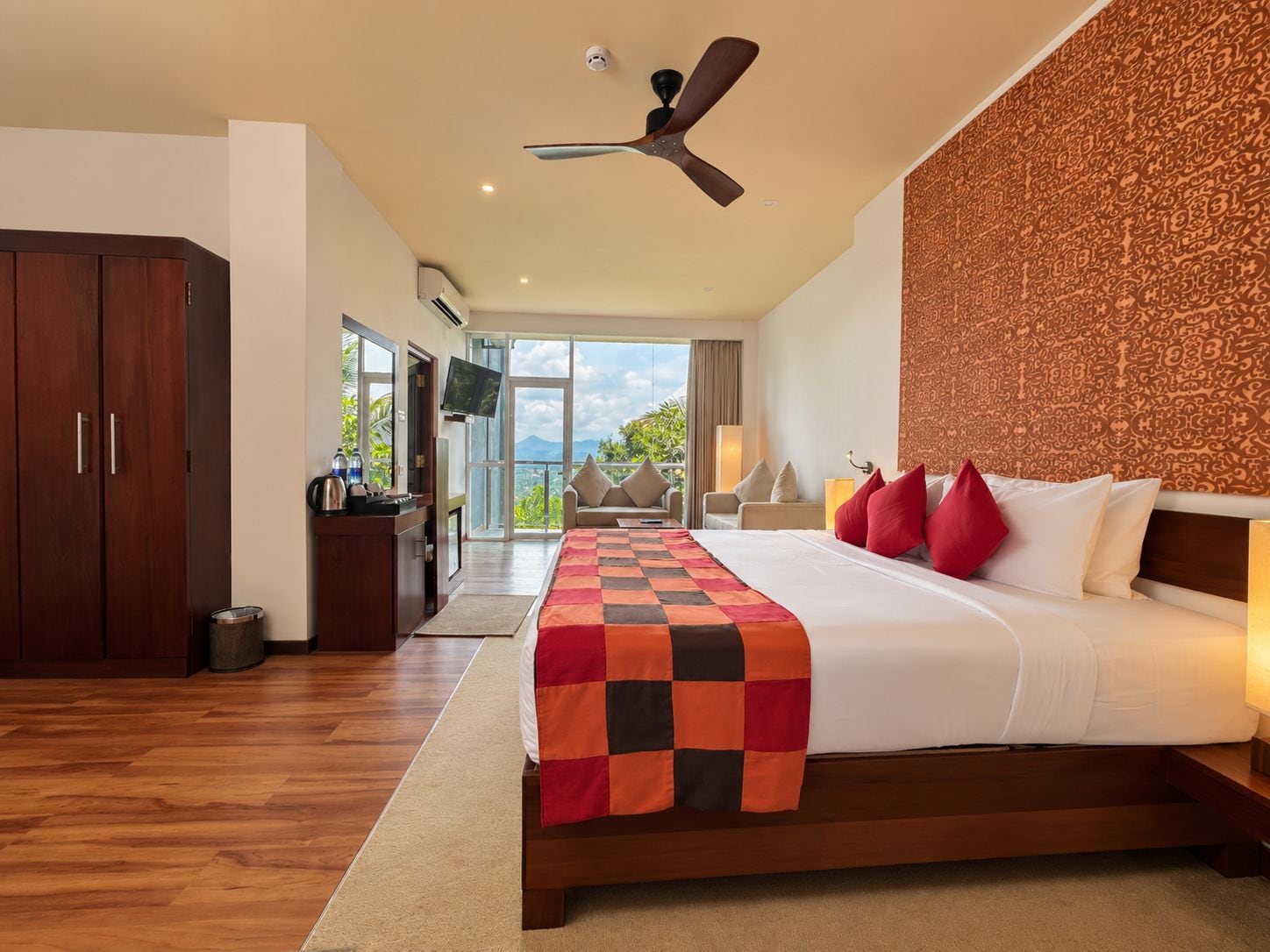 A hotel room with a bed, a desk, a ceiling fan, and a view of the outdoors.