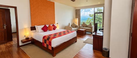A hotel room with a large bed, a desk, a chair, a sofa, a ceiling fan, and a view of the outdoors.