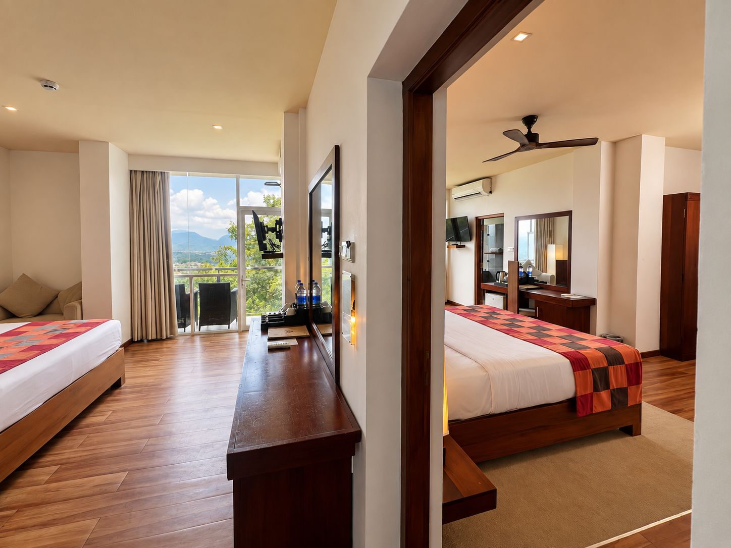 Een hotelkamer met twee bedden, een bureau, een televisie, een spiegel en een balkon met uitzicht.