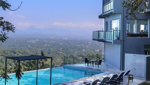 A modern hotel with a rooftop infinity pool, outdoor seating, and a scenic mountain view.