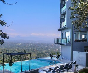A modern hotel with a rooftop infinity pool, outdoor seating, and a scenic mountain view.