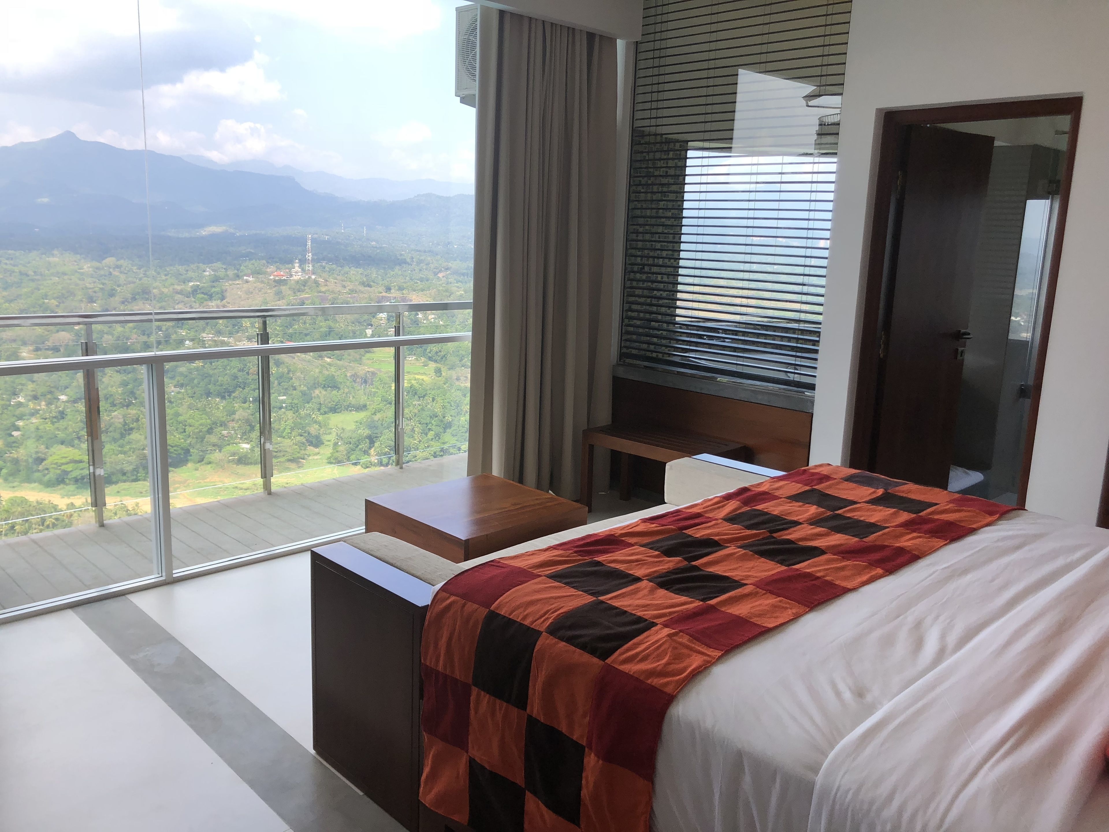 Une chambre dotée d’un grand lit, d’une table de chevet en bois, d’un bureau et offrant une vue sur un paysage montagneux grâce à de grandes fenêtres.
