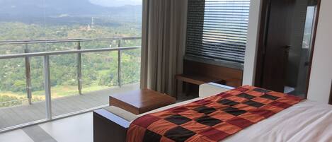 A bedroom with a large bed, a wooden nightstand, a desk, and a view of a mountainous landscape through large windows.