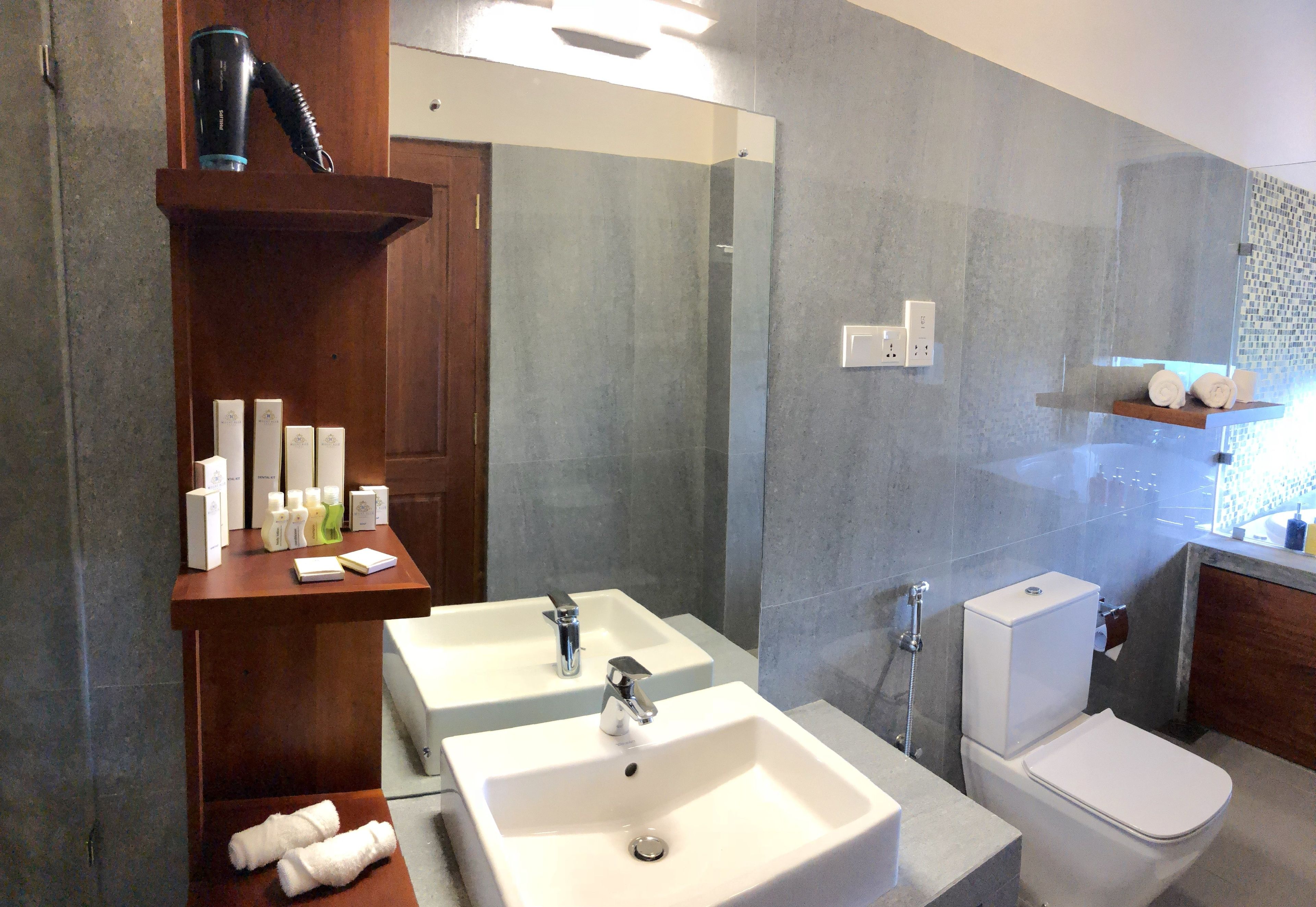 A modern bathroom with two sinks, a toilet, and a shower. There are towels and toiletries on the counter.