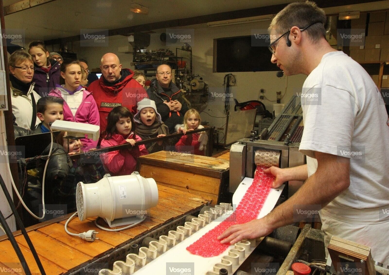 Un homme manipule une machine dans un atelier, tandis qu’un groupe d’enfants observe.