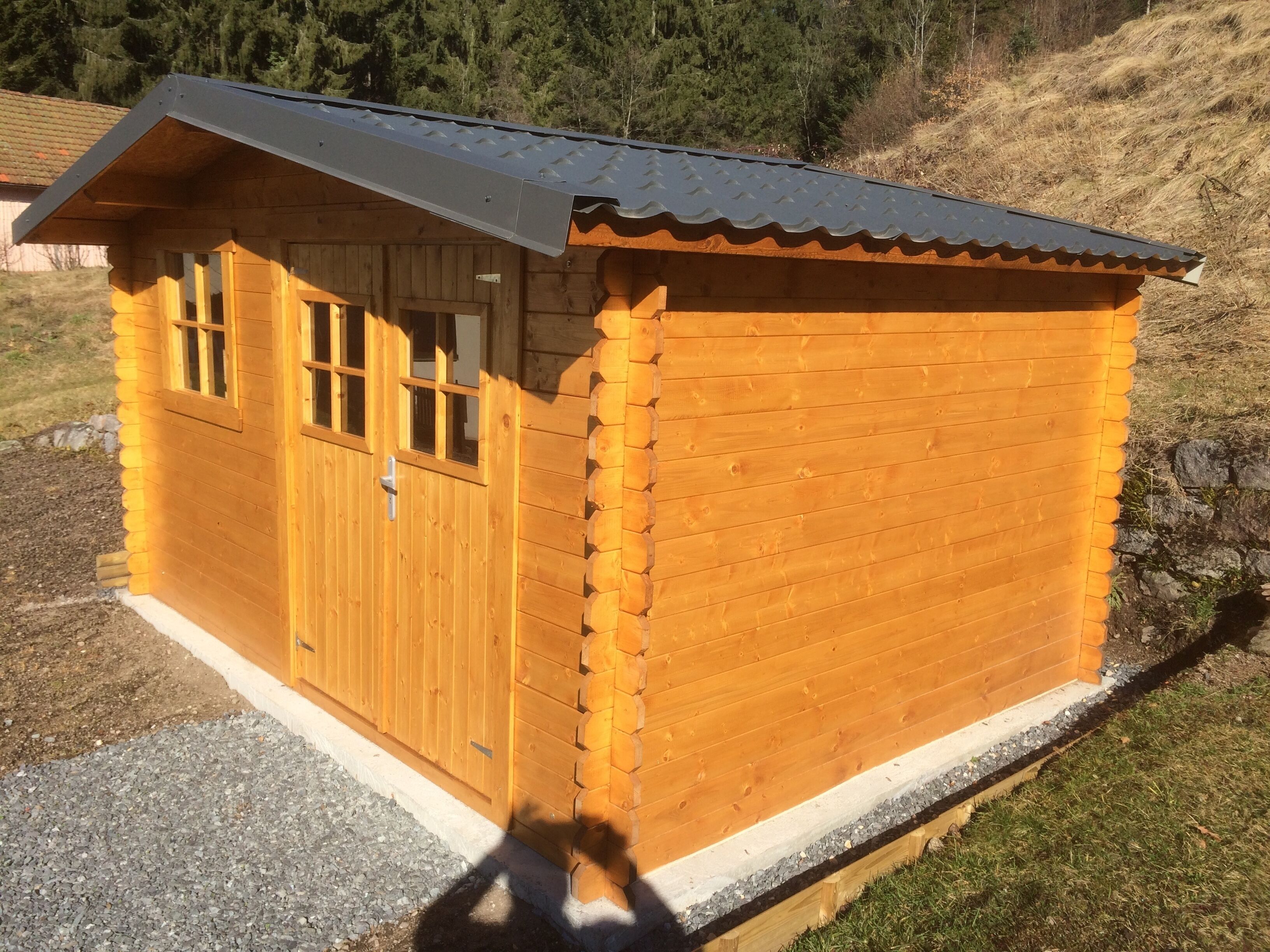 Una pequeña cabaña de madera con techo inclinado, una puerta principal y ventanas.