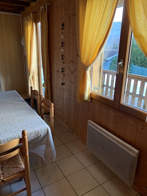 Una habitación de madera con una cama, sillas, un radiador y una ventana con cortinas.