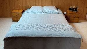 Un dormitorio con techo inclinado, paneles de madera en las paredes, una cama con ropa de cama estampada, dos mesitas de noche e iluminación fijada en la pared.