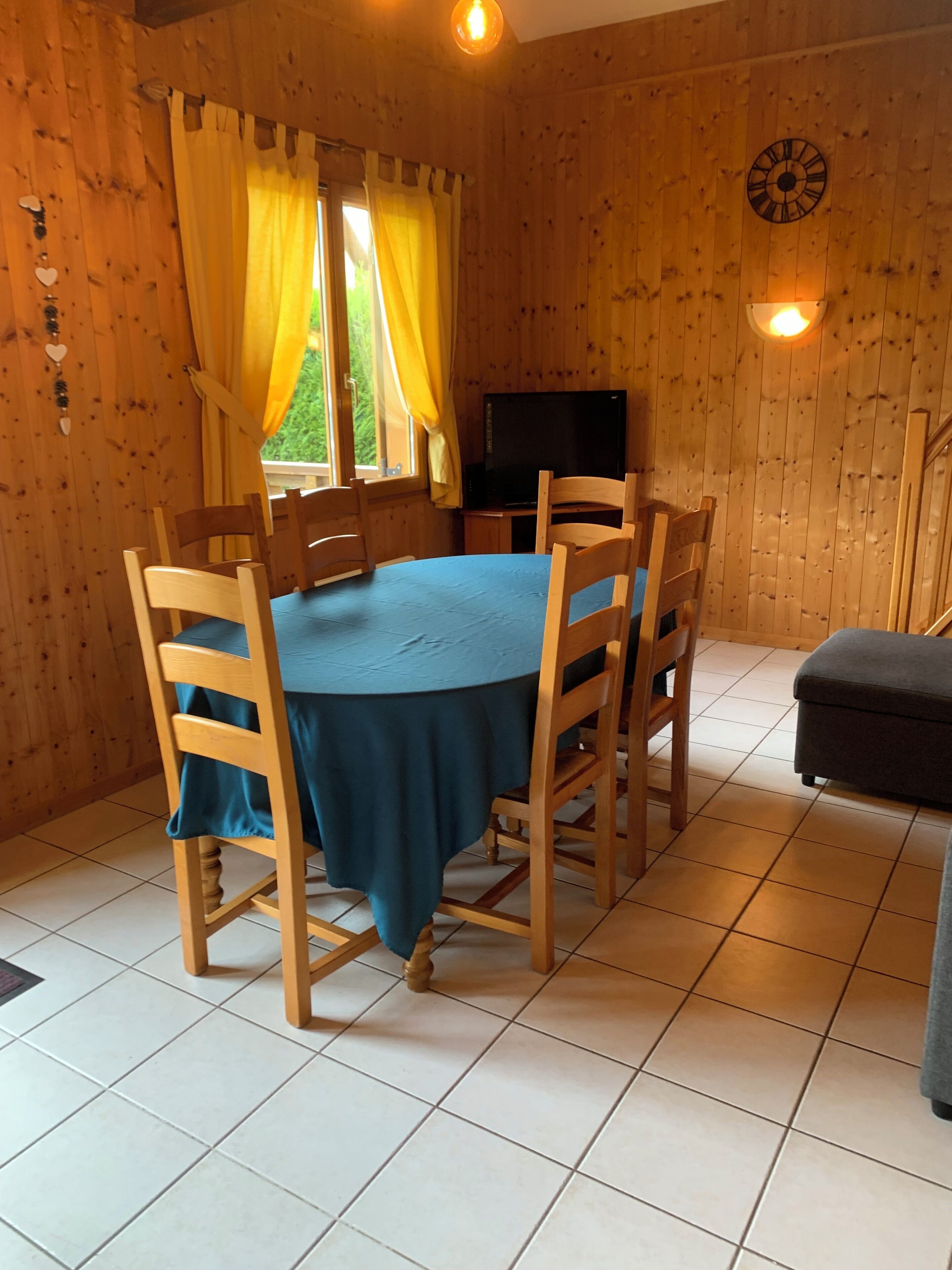 A wooden-paneled room with a round table, chairs, a television, and a clock on the wall.