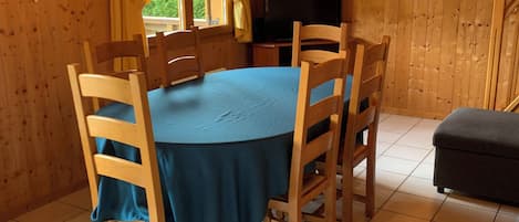 A wooden-paneled room with a round table, chairs, a television, and a clock on the wall.