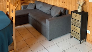 Una habitación acogedora con una escalera de madera, un sofá seccional gris, una mesita y un mueble con cajones.