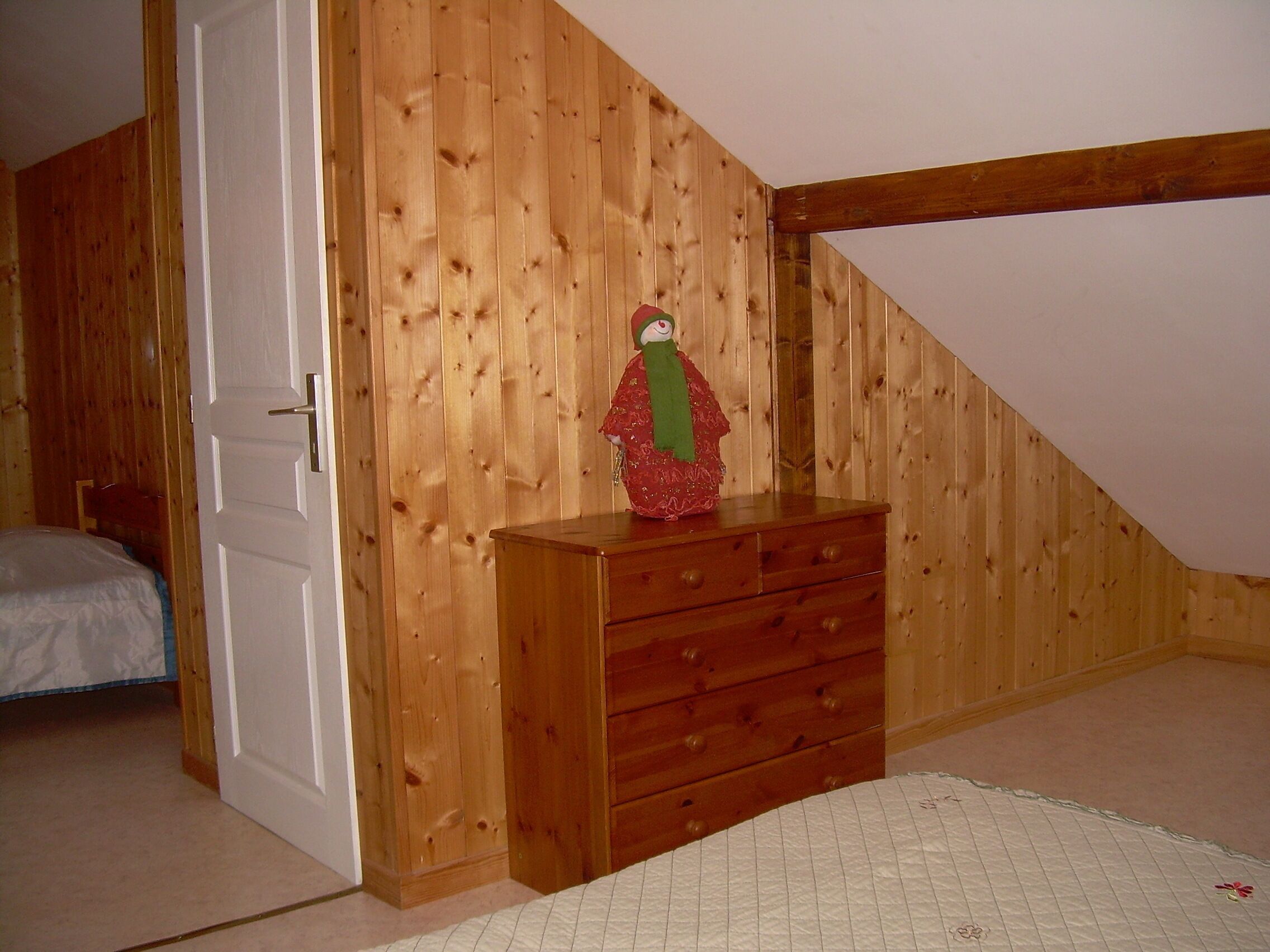 A bedroom with a wooden wardrobe, a bed with a white duvet, and a wooden door.