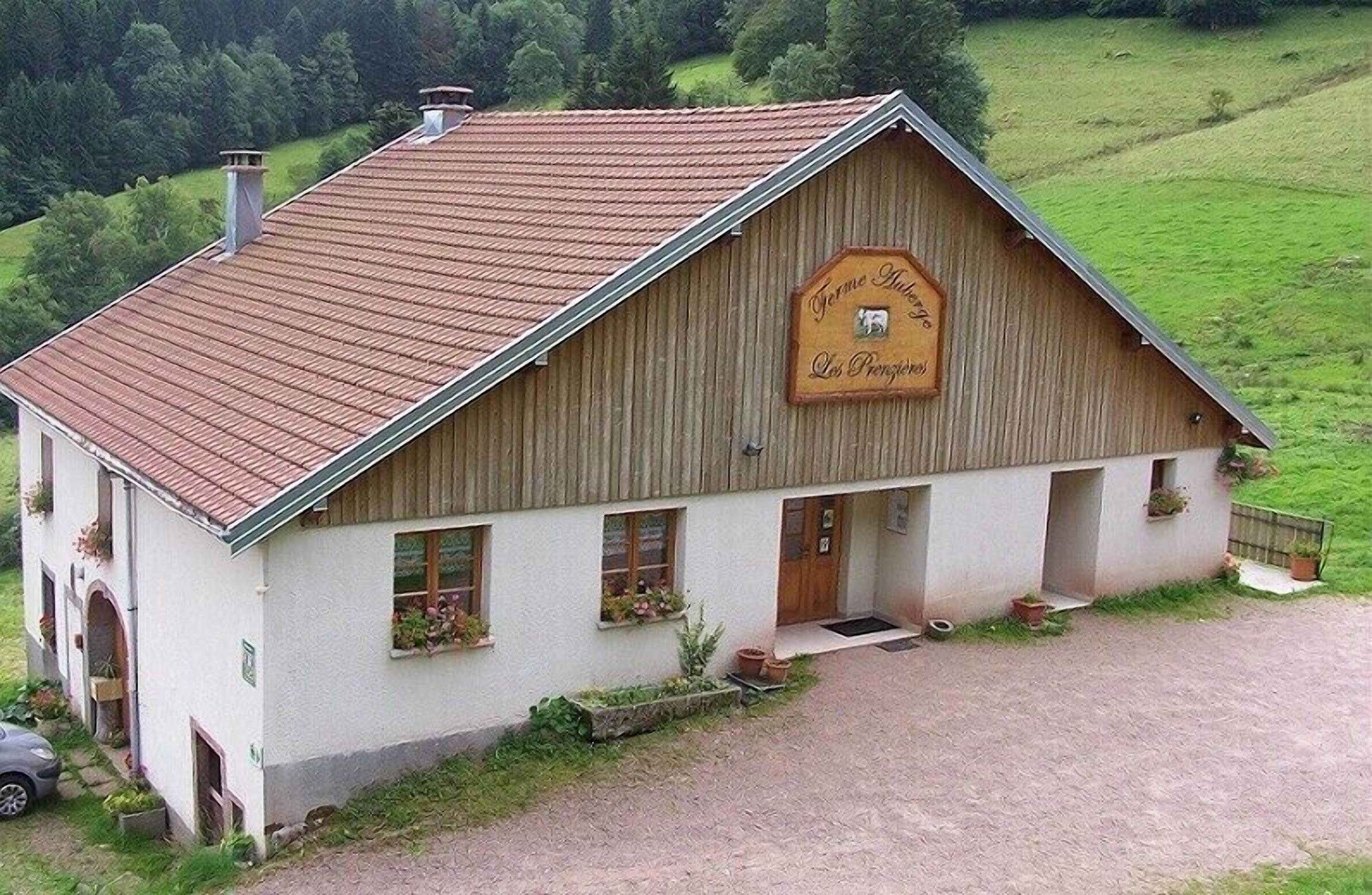 Un bâtiment de style rustique, rappelant une grange, avec un toit en pente, une enseigne en bois et un petit porche agrémenté de plantes en pot.