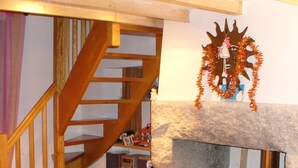 A cozy living room with a stone fireplace, wooden staircase, and a television on a shelf.