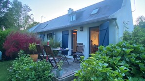 A house with a patio, a dining area with chairs, and a garden with bushes.