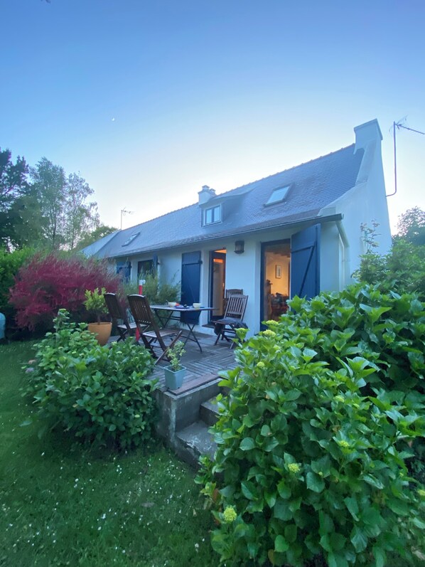 A house with a patio, a dining area with chairs, and a garden with bushes. - Old Fisherman's cottage with beautiful garden 150 m from the beaches (Concarneau)