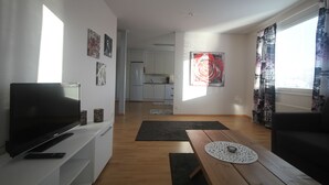 A living room with a flat-screen TV, a wooden coffee table, and a sofa. There is a kitchen in the background with white cabinets and a refrigerator. - Jääskän Loma Ratatie Apartments Kauhava (Kauhava)