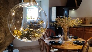 Een eetruimte met een ronde tafel, stoelen en een hanglamp met bloemen.