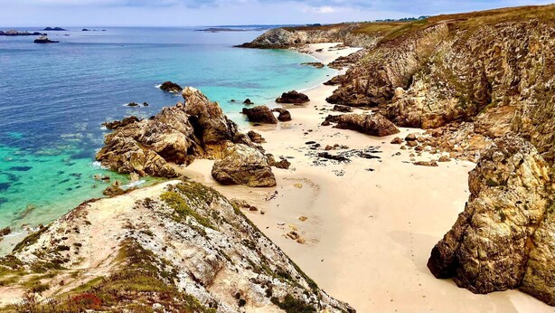 Een kustlandschap met rotsformaties, helder turquoise water en een zandstrand.