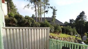 Eine Holzterrasse mit einem Metalltisch und Stühlen, umgeben von einem grünen Zaun und Bäumen.
