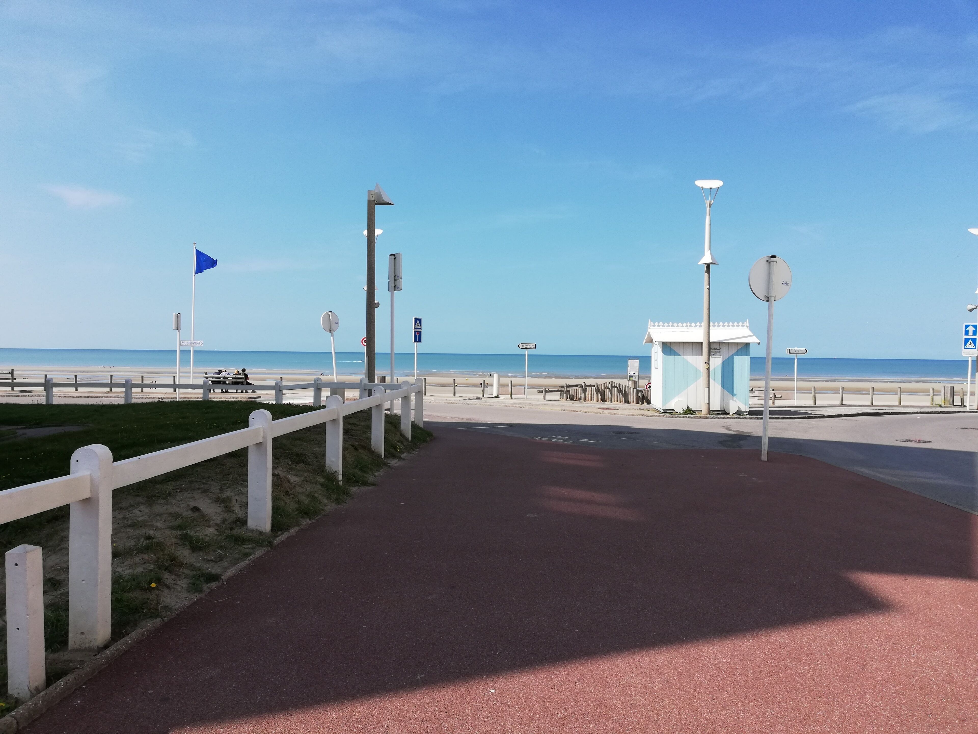 A coastal walkway with a red path, white fence, and beach in the background.