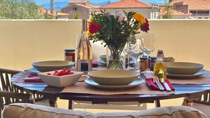 Mesa de jantar montada ao ar livre, com pratos, tigelas, um vaso de flores e diversos temperos.