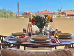 A dining table set outdoors with plates, bowls, a vase of flowers, and various condiments.