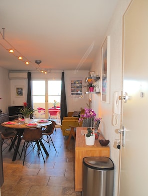 A dining area with a table and chairs, a trash bin, and a potted plant.