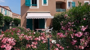 A two-story building with a balcony, a white awning, and pink flowering plants in the foreground. - Vacation home 2 bedrooms, inner courtyard, seaside, 5 places max WiFi parking (Torreilles)