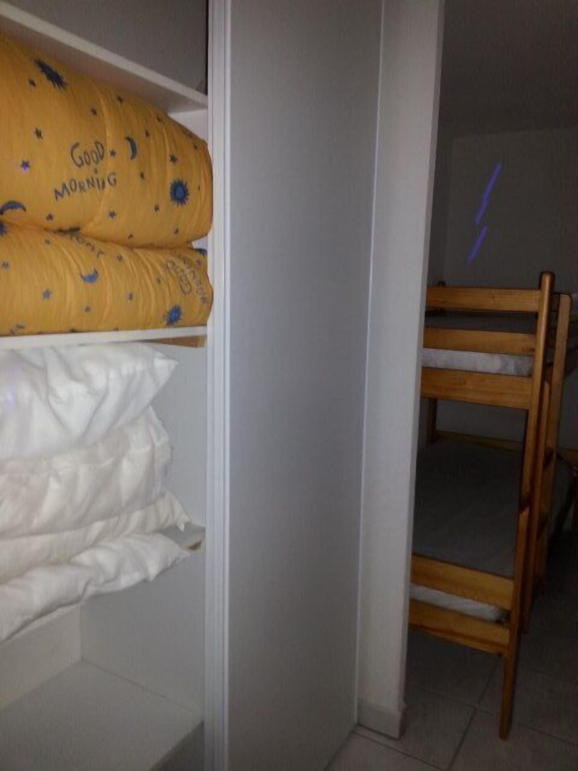 Un lit superposé avec un oreiller jaune et un oreiller blanc, une chaise en bois et un mur blanc.