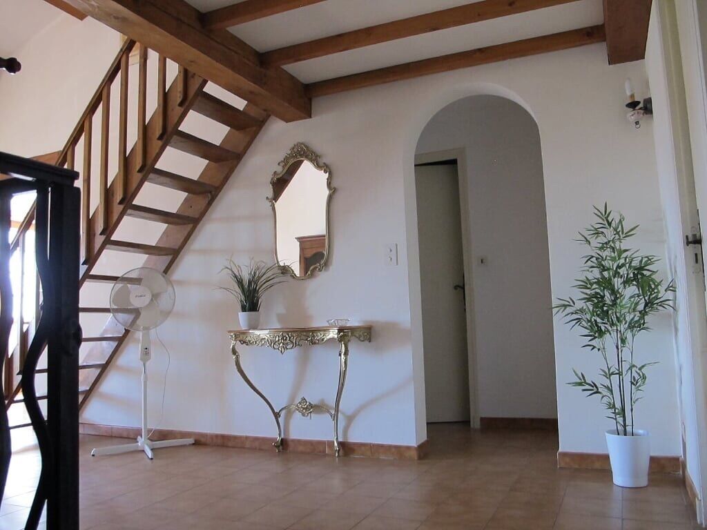 Una habitación amplia con una escalera de madera, una mesa consola blanca con una planta, un espejo grande y una planta de bambú en maceta.