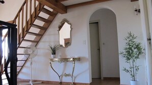 Une pièce spacieuse avec un escalier en bois, une console blanche ornée d’une plante, un grand miroir et un pot de bambou.