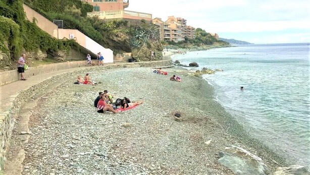 A pebbled beach with people sunbathing and swimming, a building with balconies, and a clear view of the sea. - Detached house, near the coast, in a quiet area on the outskirts of BASTIA (Ville-Di-Pietrabugno)