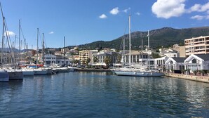A marina with boats docked, buildings in the background, and a mountain range. - Detached house, near the coast, in a quiet area on the outskirts of BASTIA (Ville-Di-Pietrabugno)