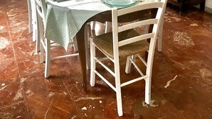 A dining area with a round table set for six, white chairs, a patterned tablecloth, and a painting on the wall. - Detached house, near the coast, in a quiet area on the outskirts of BASTIA (Ville-Di-Pietrabugno)