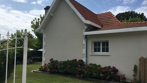 Een huis met een rood pannendak, een klein raam en een tuin met roze bloemen.