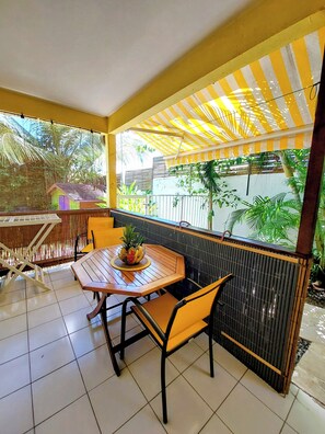 A covered patio area with a table and chairs, a bench, and a view of the outdoors.