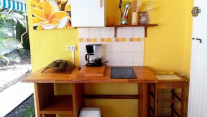 Ett litet kök med en kaffebryggare, en skål med frukt och en papperskorg.