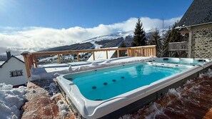 Un jacuzzi con cubierta de madera, rodeado de nieve, con vista a una montaña al fondo.