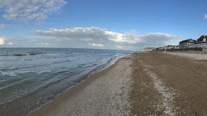 A beach with waves, a clear sky, and buildings in the background. - Beautiful renovated apartment - Walking distance to town and sea - Private parking (Cabourg)