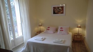 A neatly made bed with white linens and pink floral pillows, two bedside lamps, and a framed artwork above the bed.