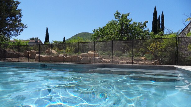A clear swimming pool with a view of a stone wall, trees, and a distant hill.