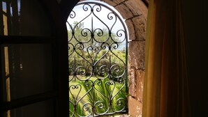 Un portail en fer forgé orné de motifs décoratifs, qui donne accès à un jardin verdoyant bordé d’un mur en pierre.