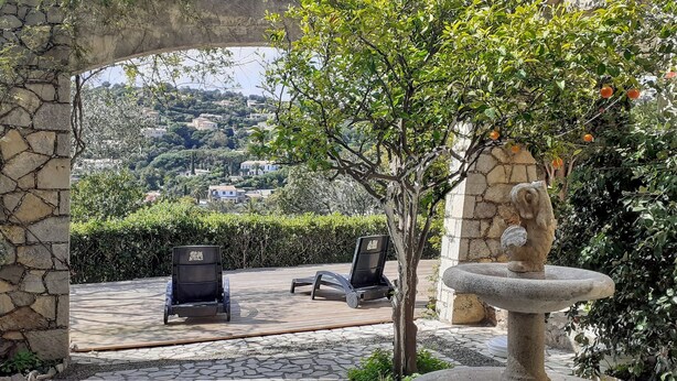Un espace extérieur aménagé avec des piliers en pierre, une fontaine en pierre et une vue sur une colline parsemée de bâtiments.