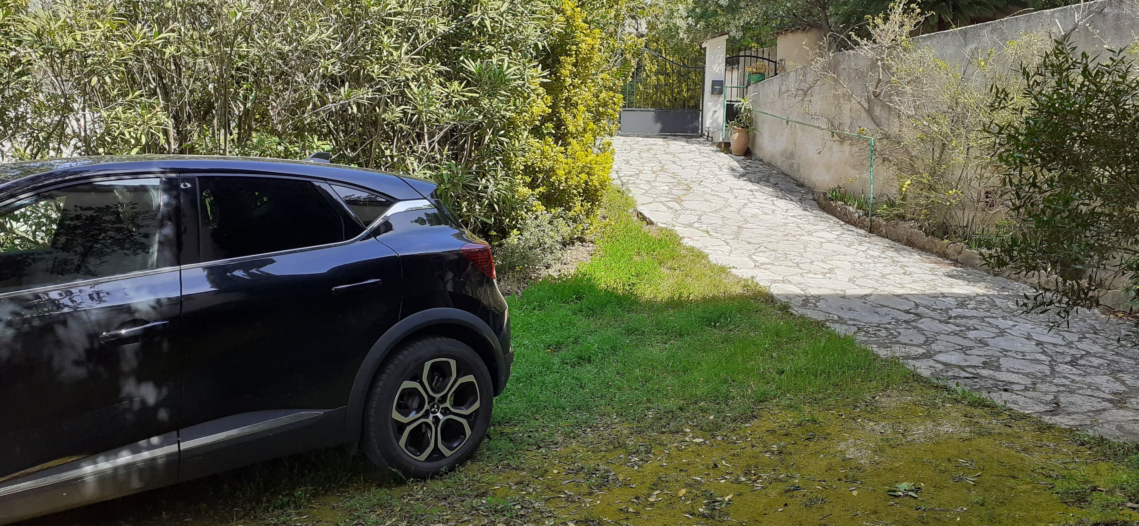 Ein schwarzes Auto steht in einem Garten, wobei ein Steinweg zu einem Tor führt.