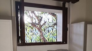 Un lit avec une literie à motifs, une fenêtre ornée de barreaux en fer décoratifs et une vue sur les arbres à l’extérieur.