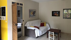 A room with a bed, a small table, and a chair. There is a door leading to another room.