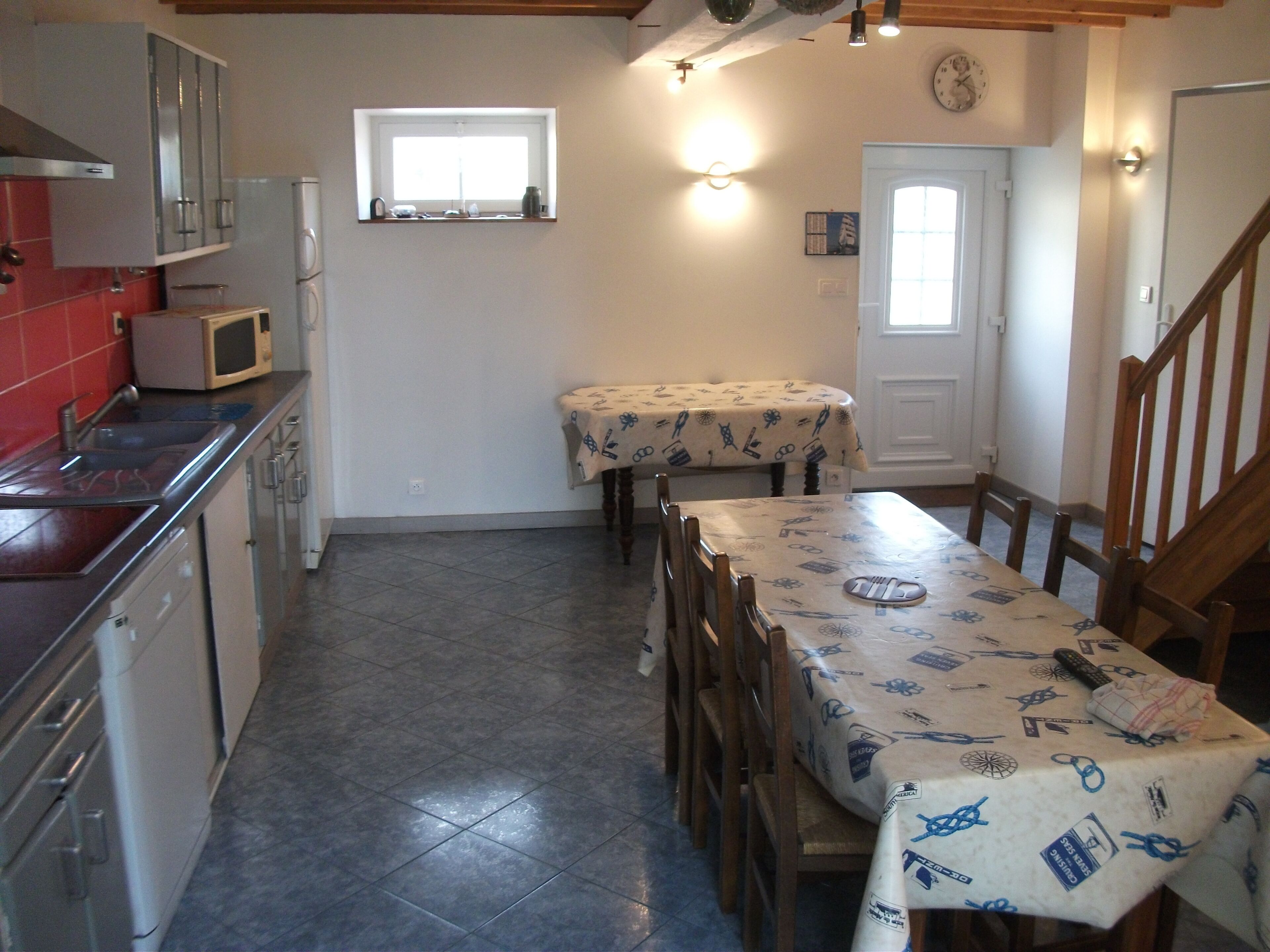 Cozinha com área de jantar, incluindo uma mesa com toalha, cadeiras, micro-ondas e frigorífico.
